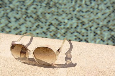 Stylish sunglasses near outdoor swimming pool on sunny day, space for text