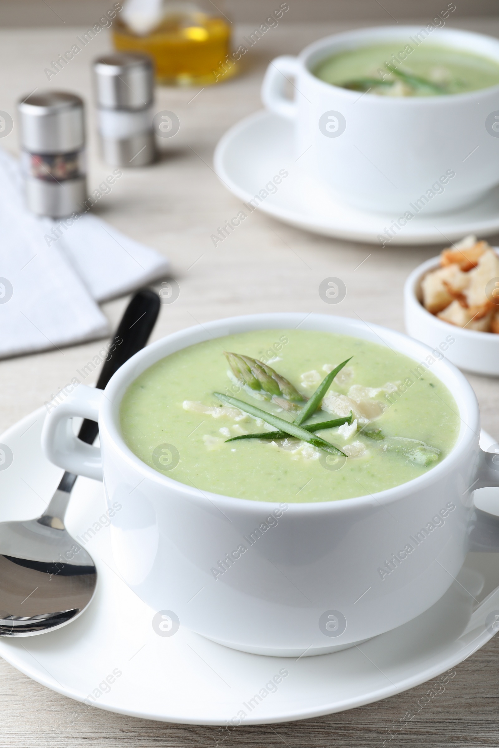 Photo of Delicious asparagus soup with green onion served on white wooden table