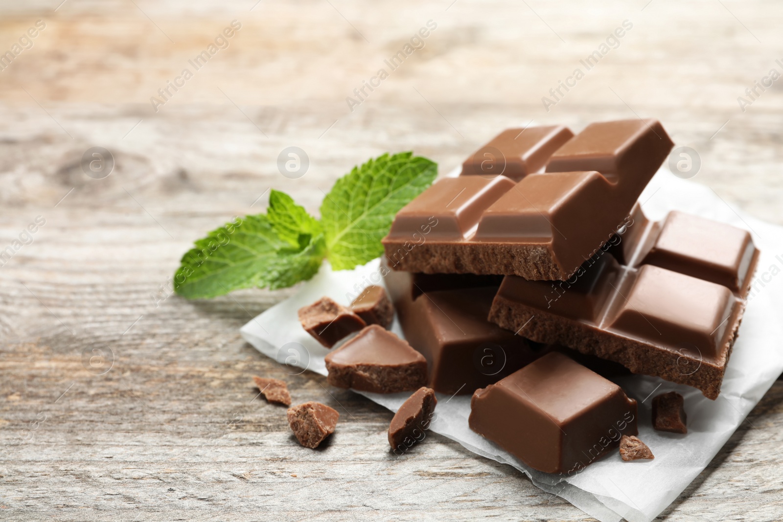 Photo of Pieces of milk chocolate with mint on wooden table