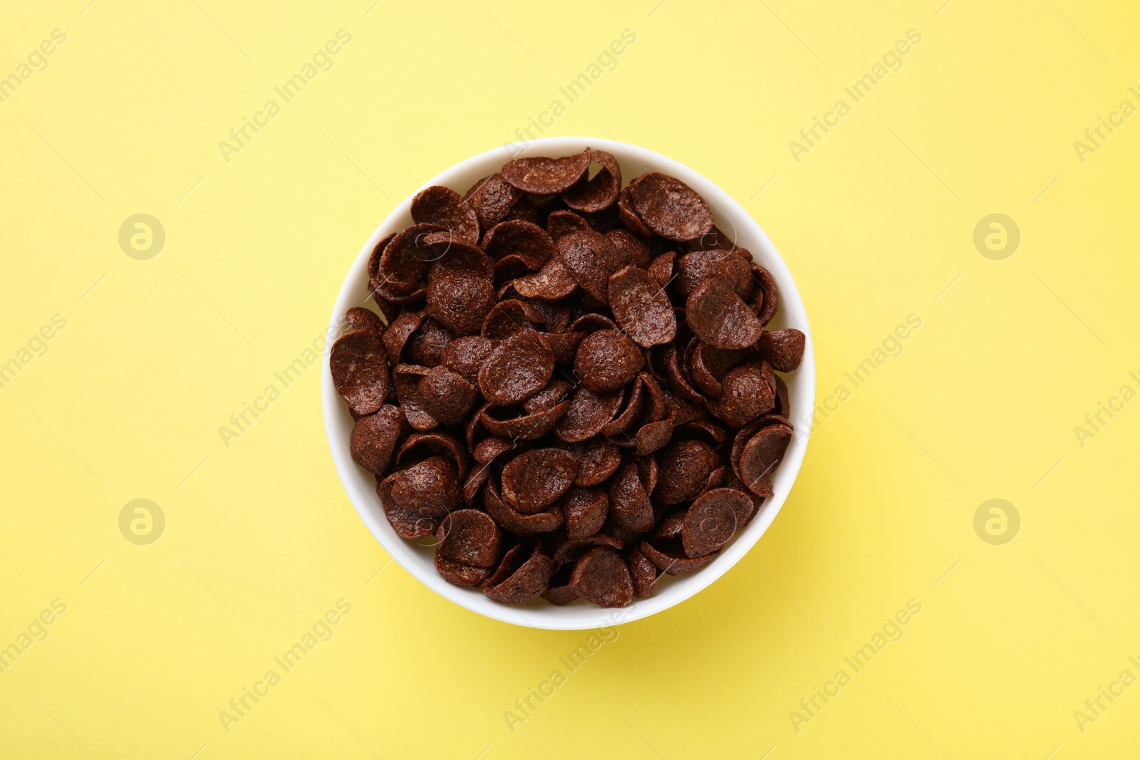 Photo of Breakfast cereal. Chocolate corn flakes in bowl on yellow table, top view