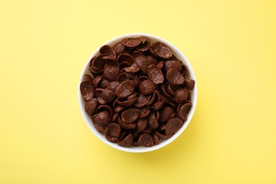 Photo of Breakfast cereal. Chocolate corn flakes in bowl on yellow table, top view