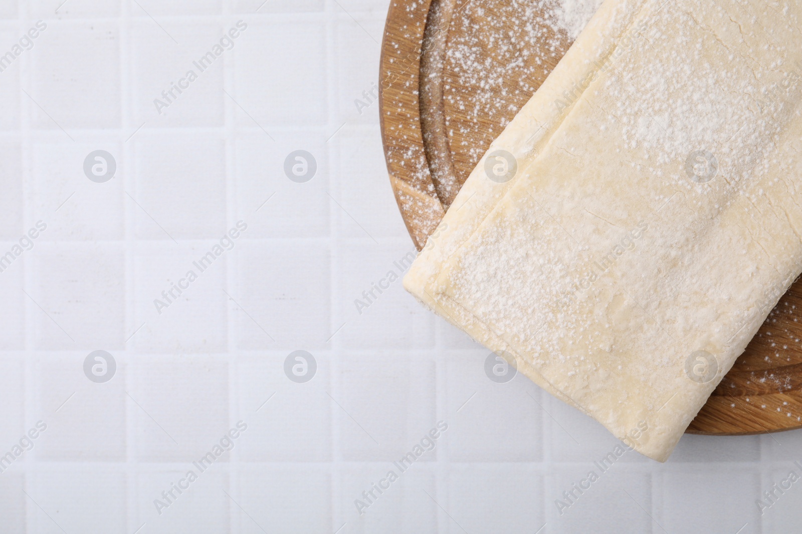 Photo of Raw puff pastry dough on white tiled table, top view. Space for text