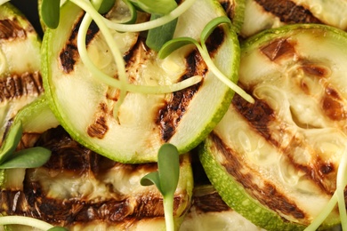 Photo of Delicious grilled zucchini slices and microgreens as background, top view