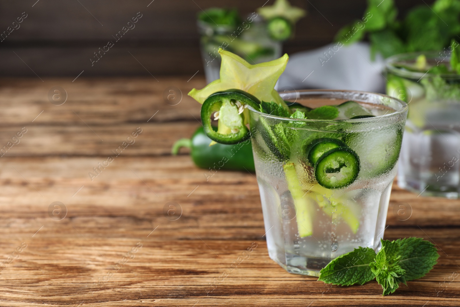 Photo of Spicy cocktail with jalapeno, carambola and mint on wooden table. Space for text