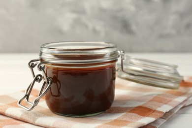 Photo of Tasty barbecue sauce in glass jar on white wooden table, closeup