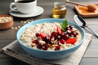 Photo of Bowl of oatmeal porridge served with berries on wooden table
