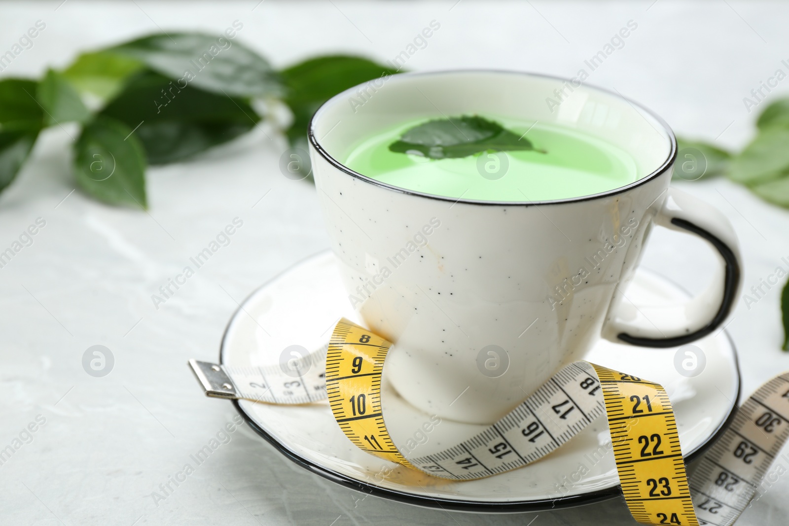 Photo of Cup of herbal diet tea and measuring tape on light table