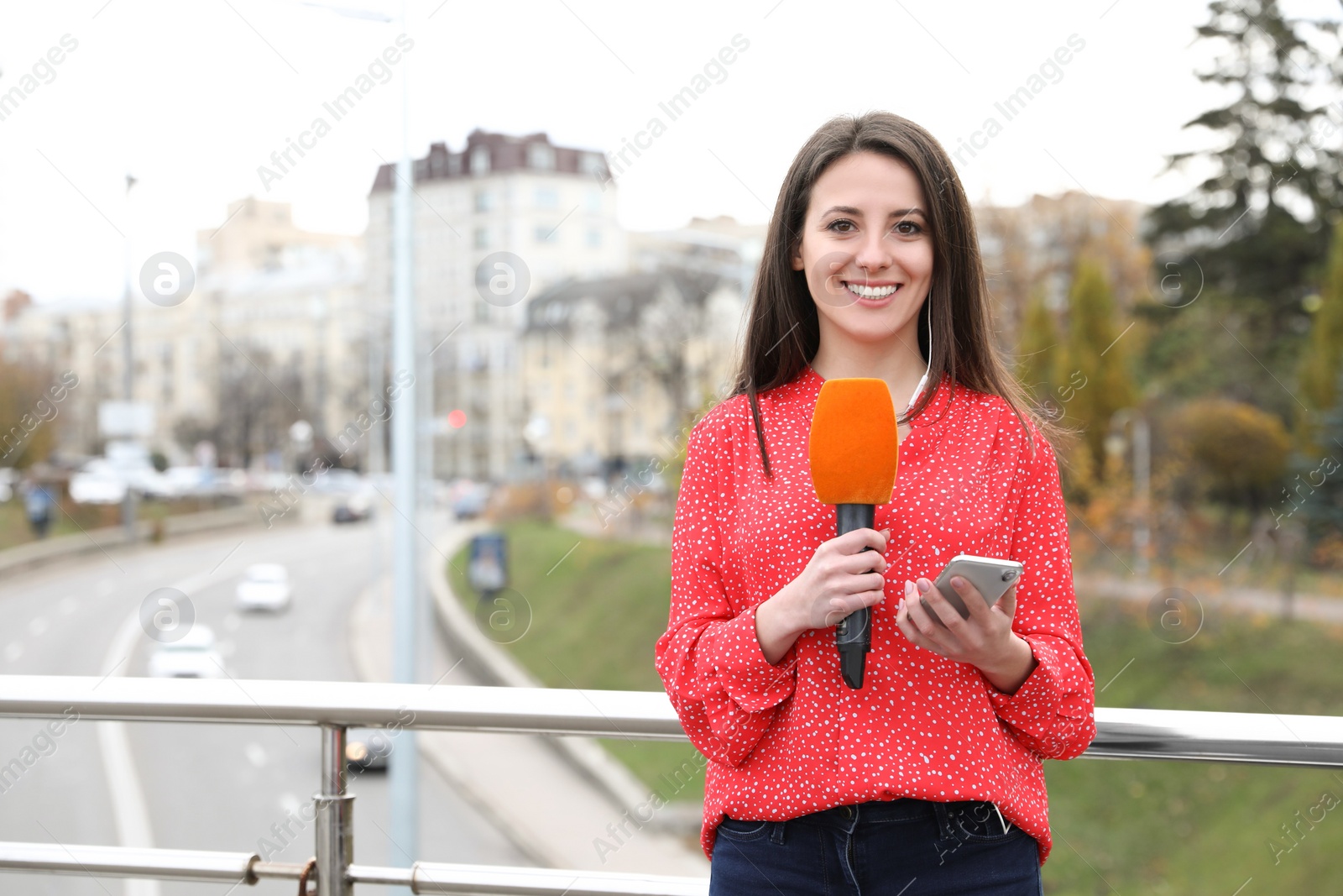 Photo of Young female journalist with microphone and smartphone working on city street. Space for text