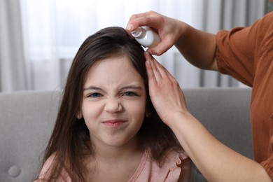 Mother using lice treatment spray on her daughter's hair indoors