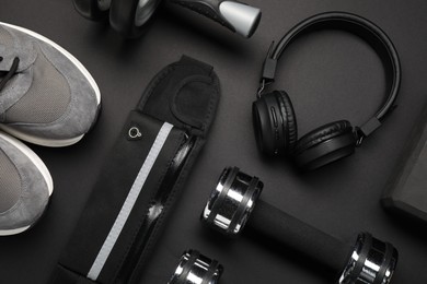 Photo of Sports equipment, headphones and sneakers on black background, flat lay