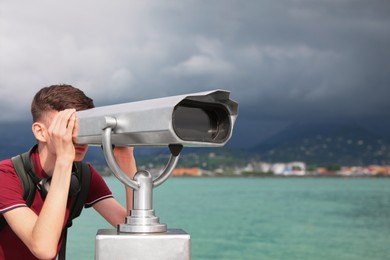 Photo of Teenage boy looking through mounted binoculars near sea. Space for text