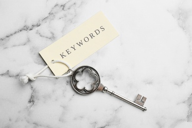 Vintage key and tag wIth word KEYWORDS on white marble table, top view