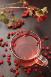 Cup with hawthorn tea and berries on wooden table, above view