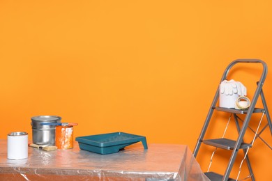 Photo of Can with paint, brush and renovation equipment on table against orange background. Space for text