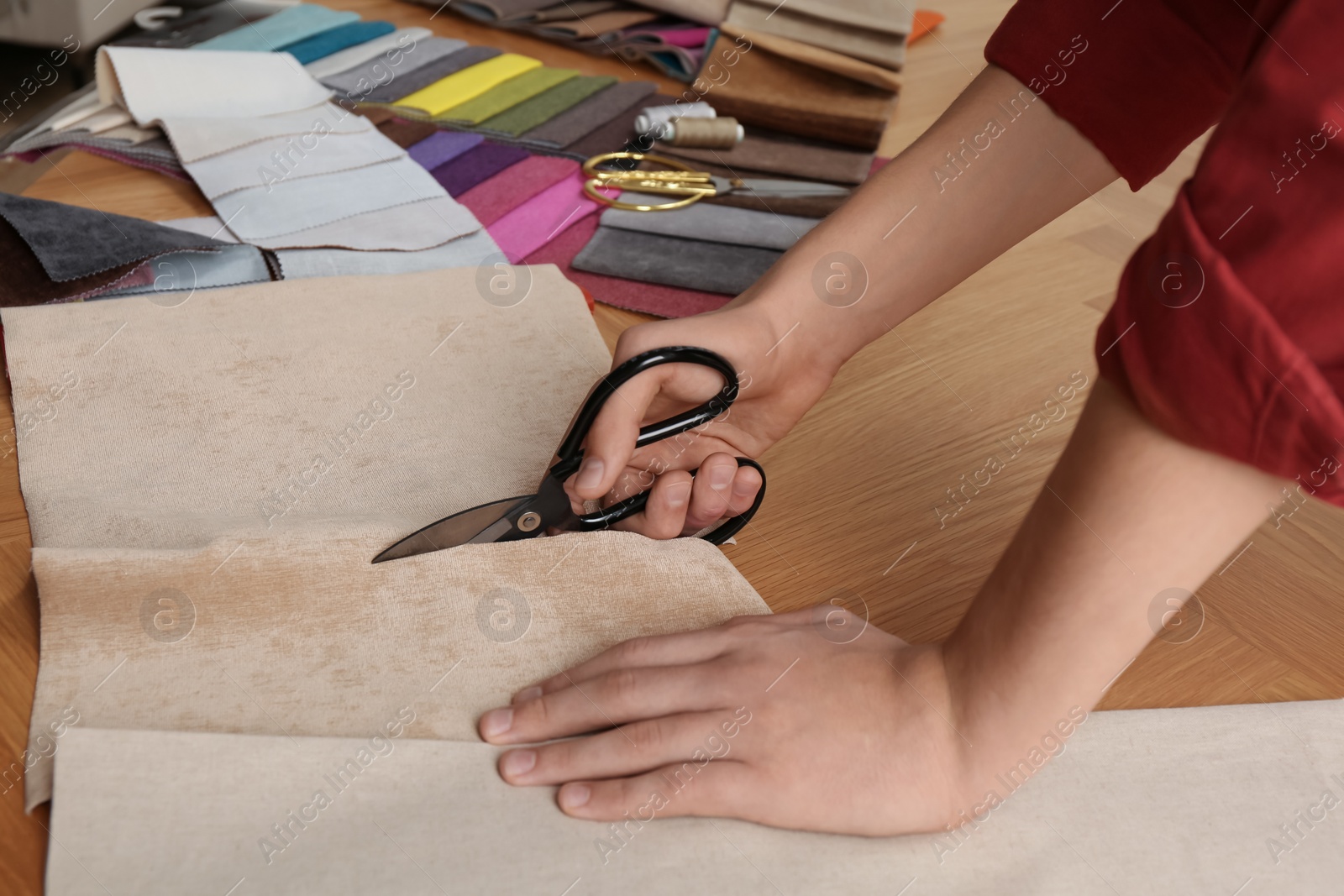 Photo of Man cutting beige fabric with scissors at wooden table, closeup