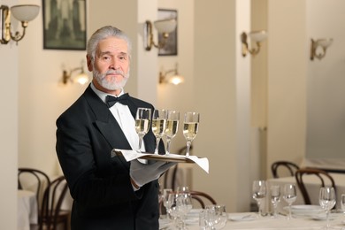 Photo of Senior butler holding tray with glasses of sparkling wine in restaurant. Space for text