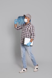 Photo of Courier in medical mask with bottle for water cooler and clipboard on light grey background. Delivery during coronavirus quarantine