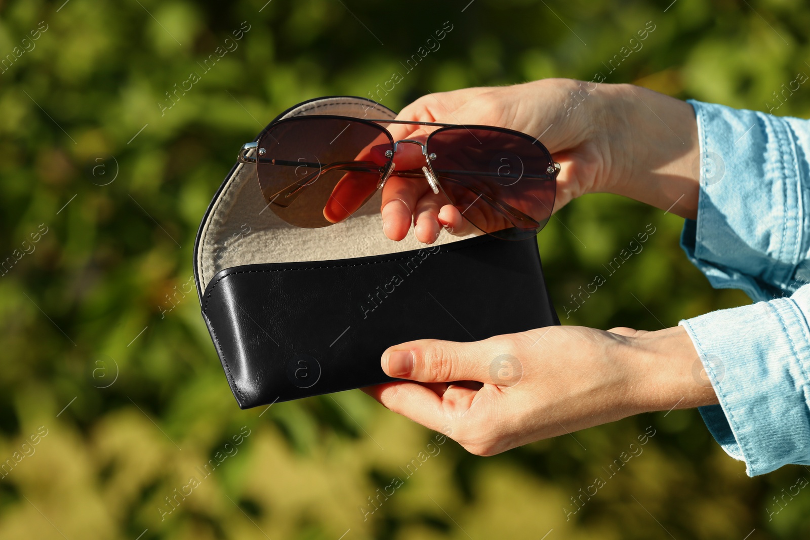 Photo of Woman holding sunglasses and case outdoors on sunny day, closeup