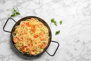 Photo of Frying pan with spaghetti and shrimps on light background, top view