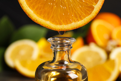 Photo of Citrus essential oil dripping from orange slice into bottle, closeup