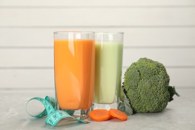 Tasty shakes, vegetables and measuring tape on light gray marble table. Weight loss