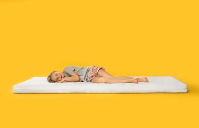 Photo of Little girl sleeping on comfortable mattress against orange background, space for text