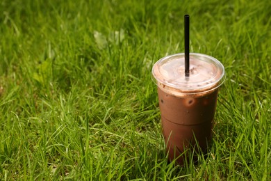 Photo of Takeaway plastic cup with cold coffee drink and straw on green grass outdoors, space for text