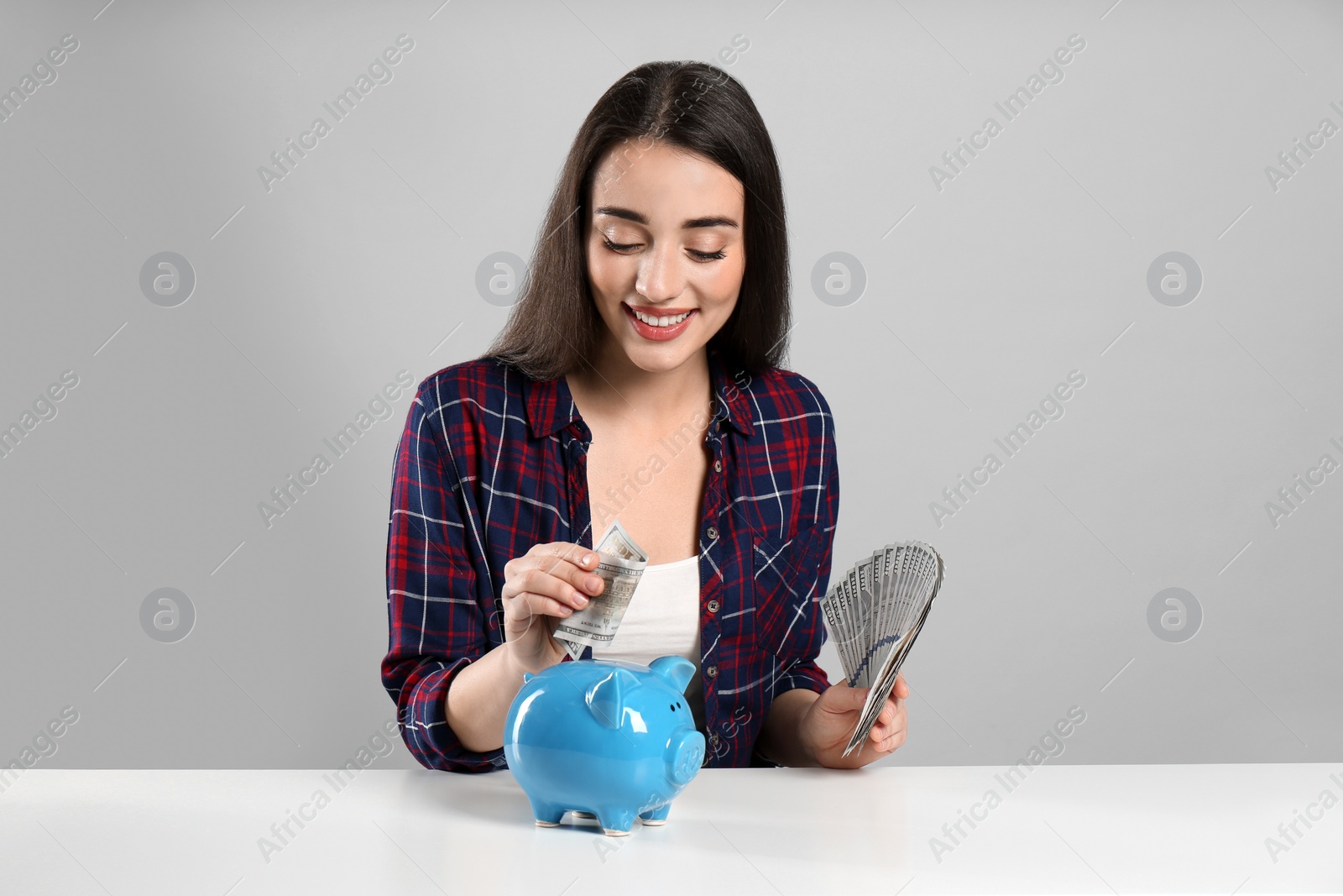 Photo of Young woman putting money into piggy bank at table on light grey background