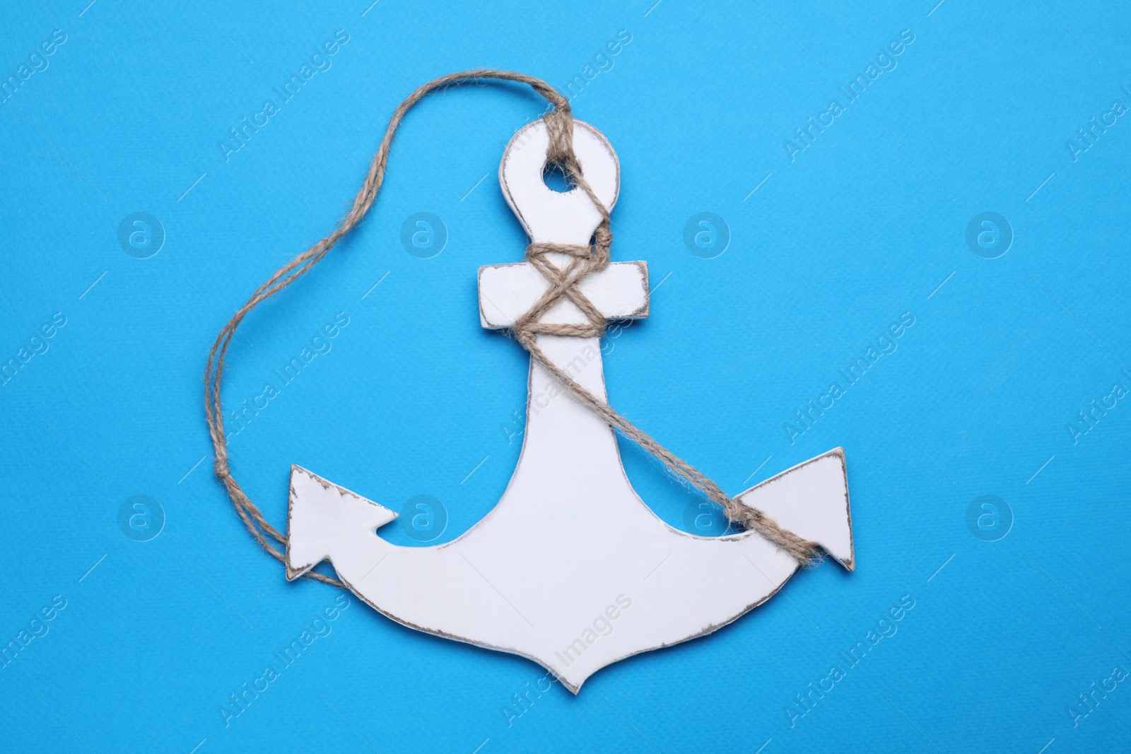 Photo of White anchor with hemp rope on light blue background, top view