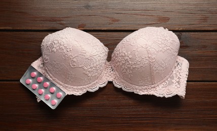Photo of Bra and pills on wooden table, flat lay. Breast cancer awareness