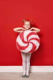 Cute little girl dressed as candy near red wall. Christmas suit