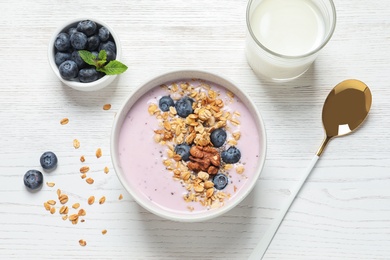 Bowl of tasty oatmeal with blueberries and yogurt on white wooden table, flat lay