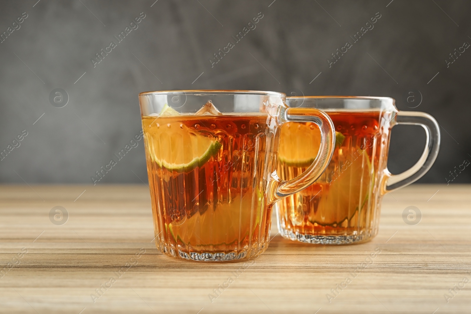 Photo of Cups of tasty ice tea with lime on wooden table against grey background