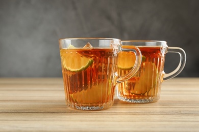 Photo of Cups of tasty ice tea with lime on wooden table against grey background