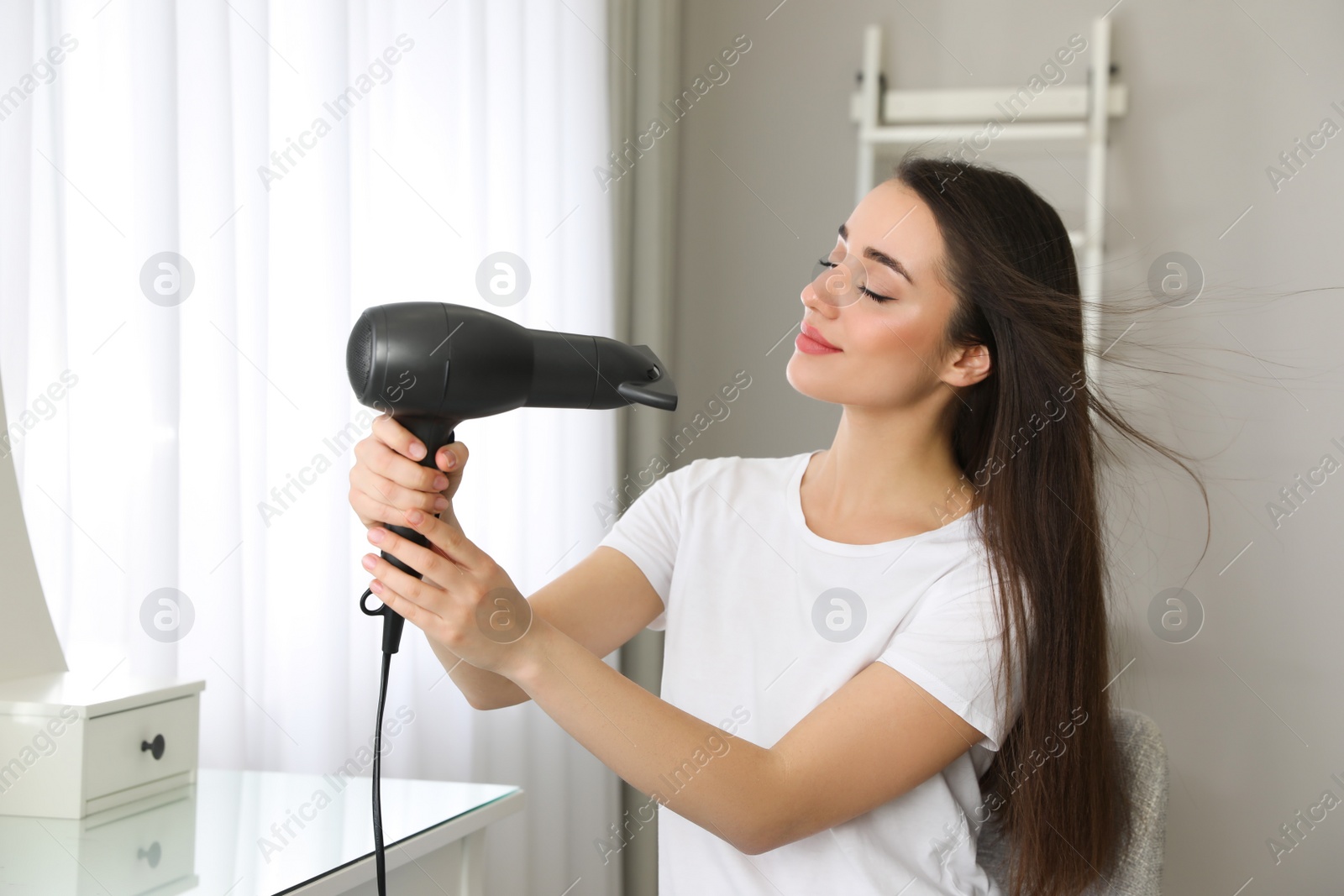 Photo of Beautiful young woman using hair dryer at home