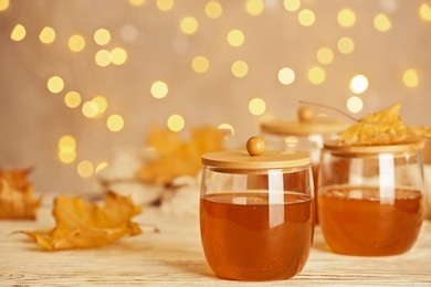 Glass jars with sweet honey on table against blurred lights. Space for text