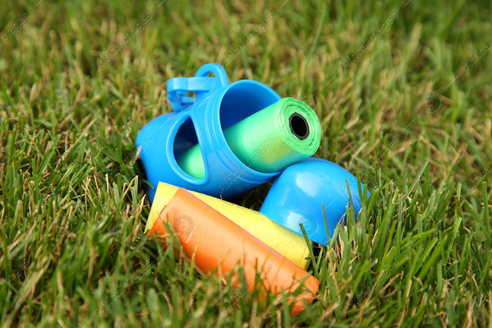 Photo of Rolls of colorful dog waste bags on green grass outdoors