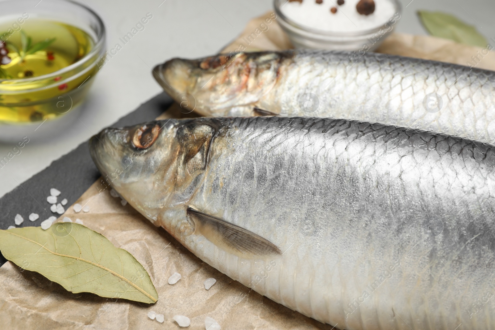 Photo of Slate plate with salted herrings, oil and spices on grey table, closeup