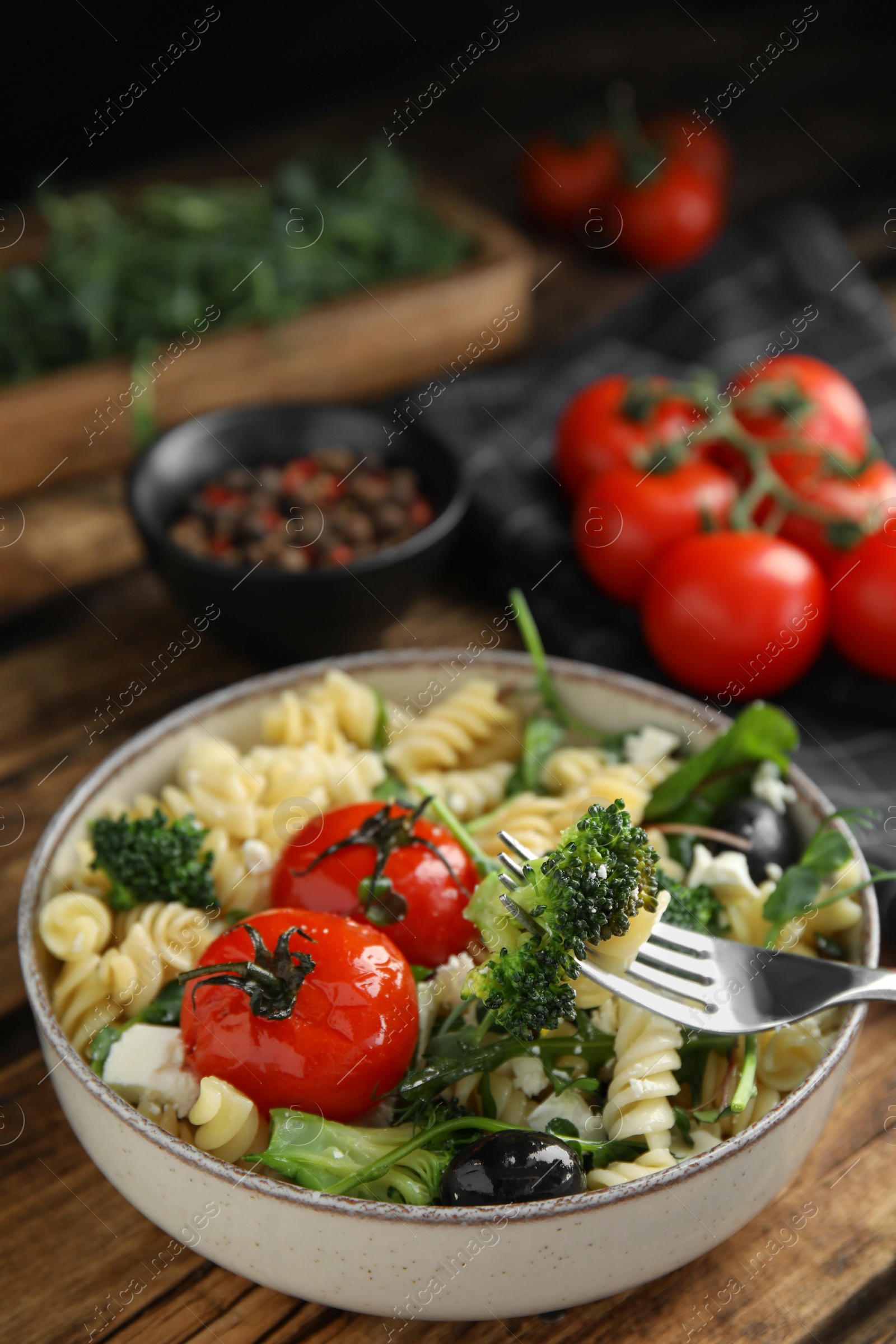 Photo of Bowl of delicious pasta with tomatoes, broccoli and cheese on wooden table