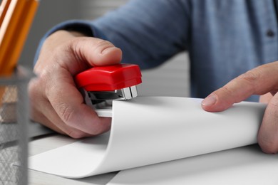 Photo of Man with papers using stapler at white table, closeup