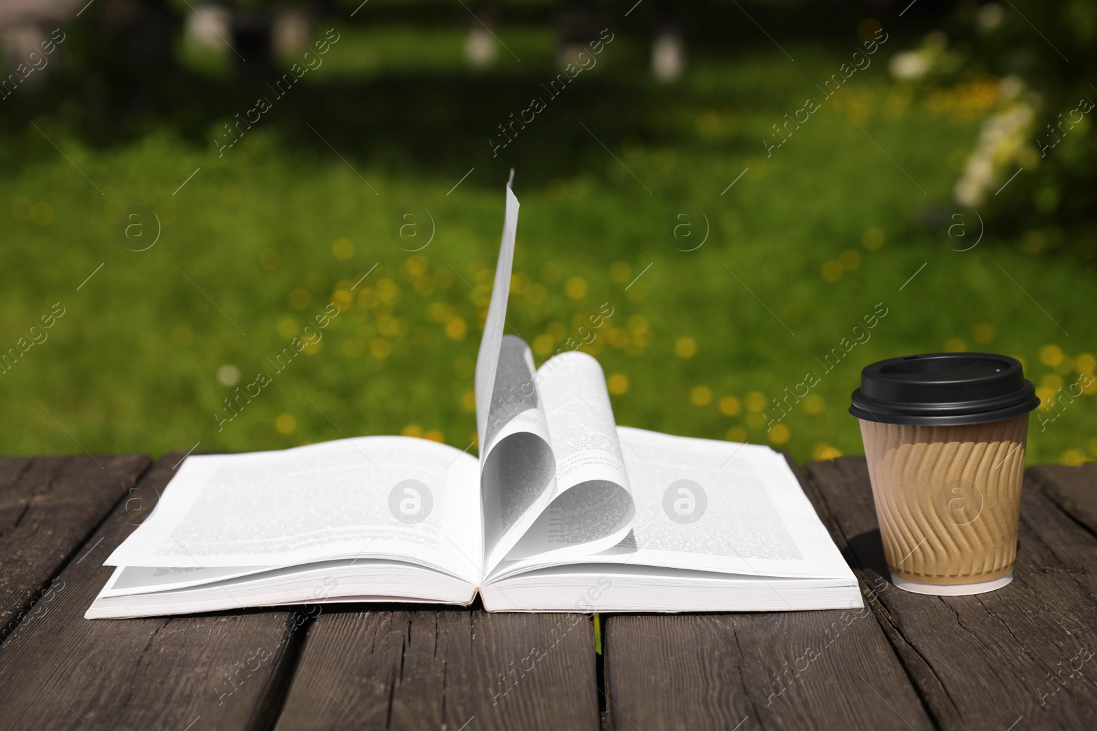 Photo of Open book and paper coffee cup on wooden table outdoors