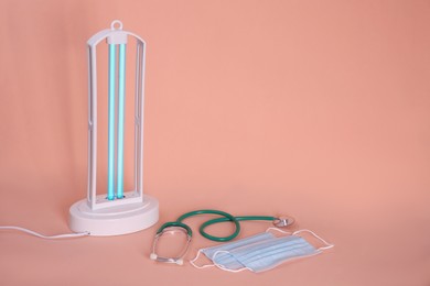 Photo of Ultraviolet lamp, medical masks and stethoscope on peach background, space for text