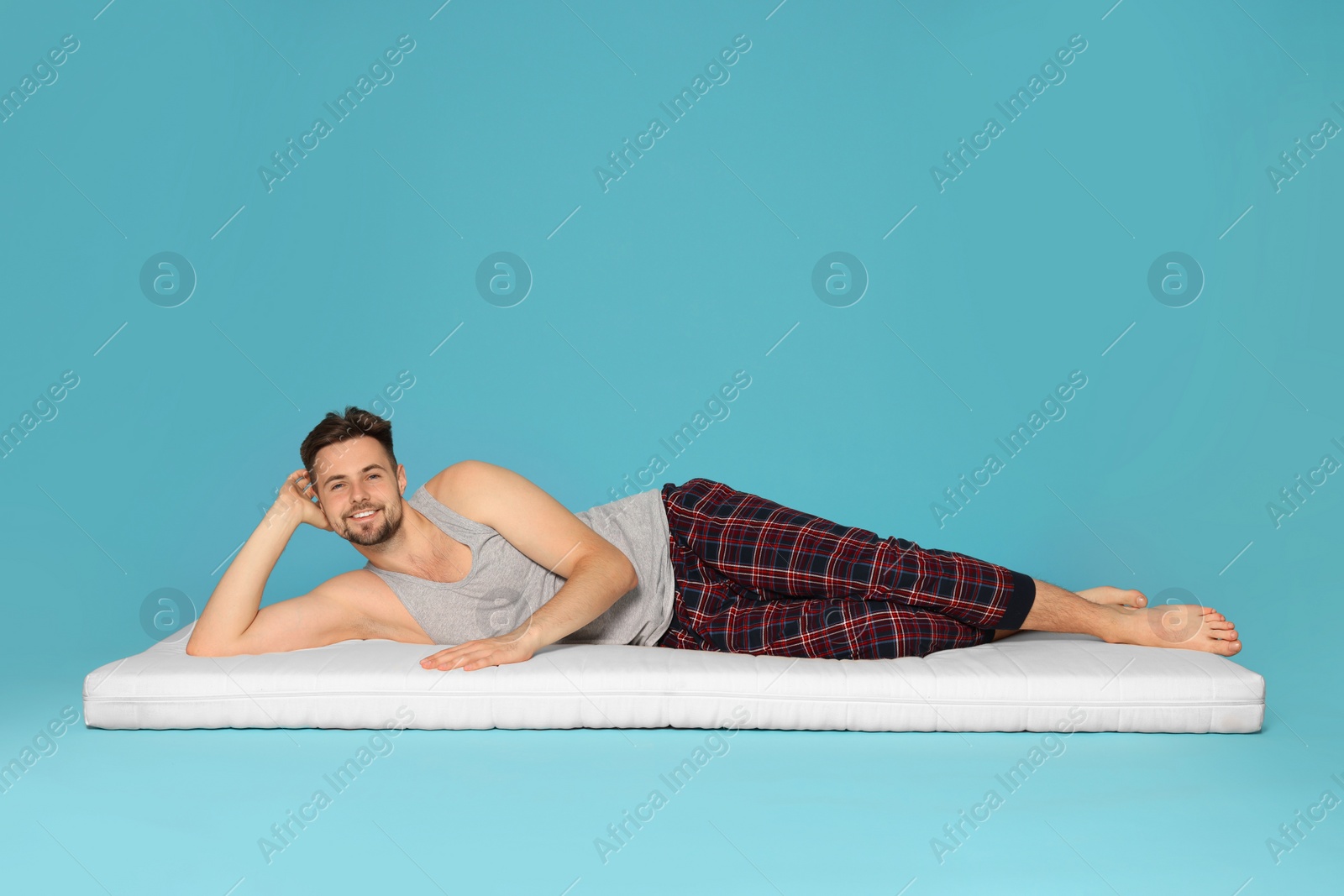 Photo of Man lying on soft mattress against light blue background