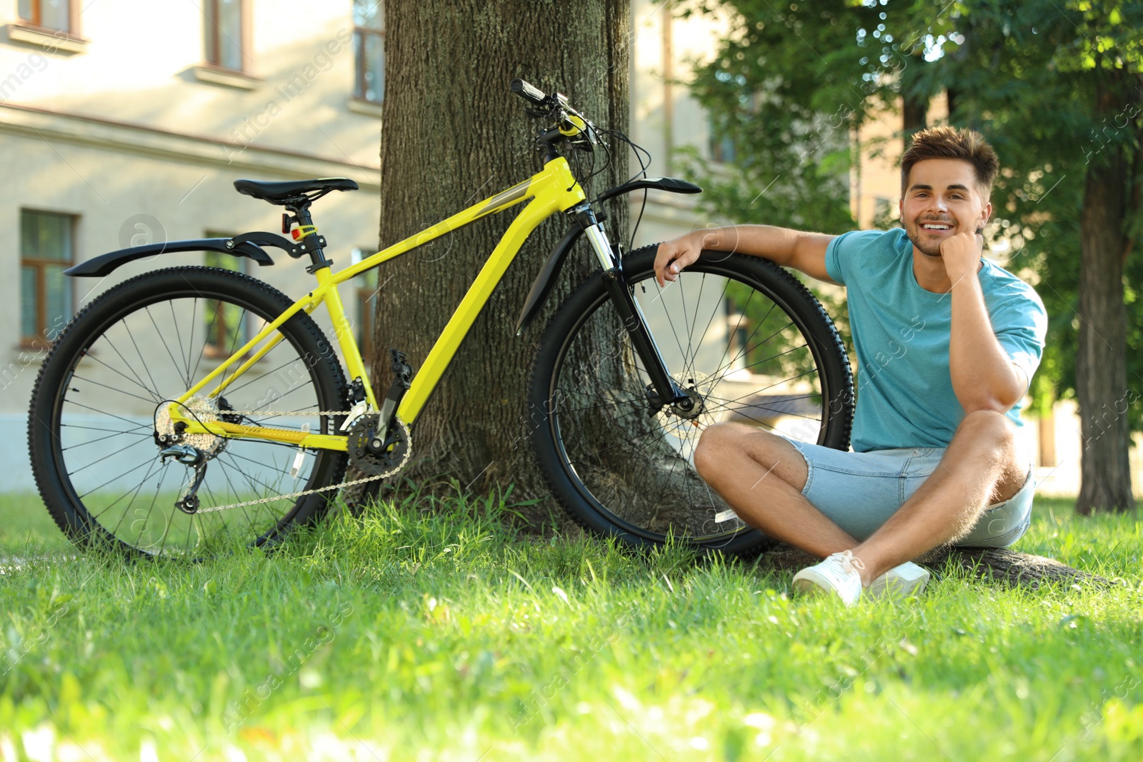 Photo of Handsome young man sitting near bicycle on green grass