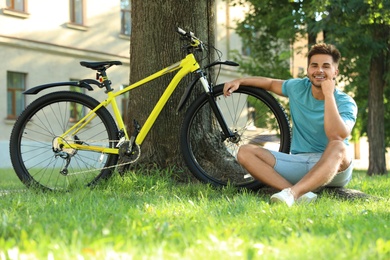 Handsome young man sitting near bicycle on green grass