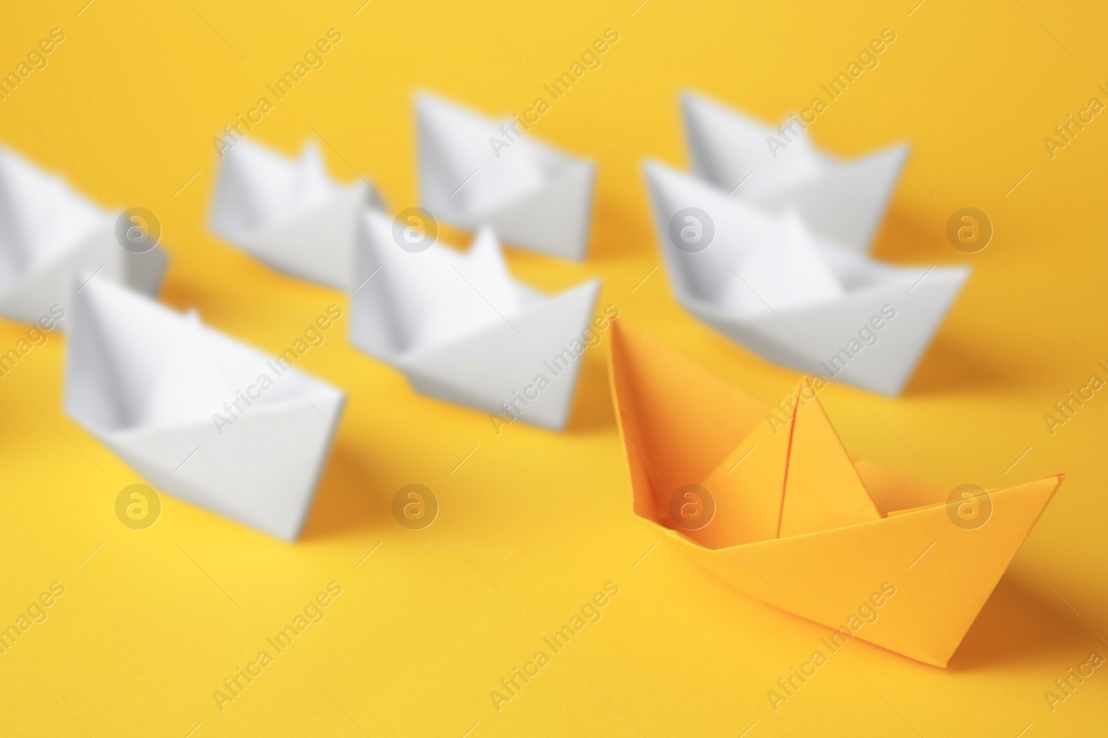 Photo of Group of paper boats following yellow one on color background. Leadership concept