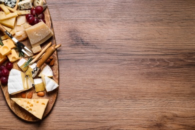 Cheese plate with rosemary, grapes and nuts on wooden table, top view. Space for text