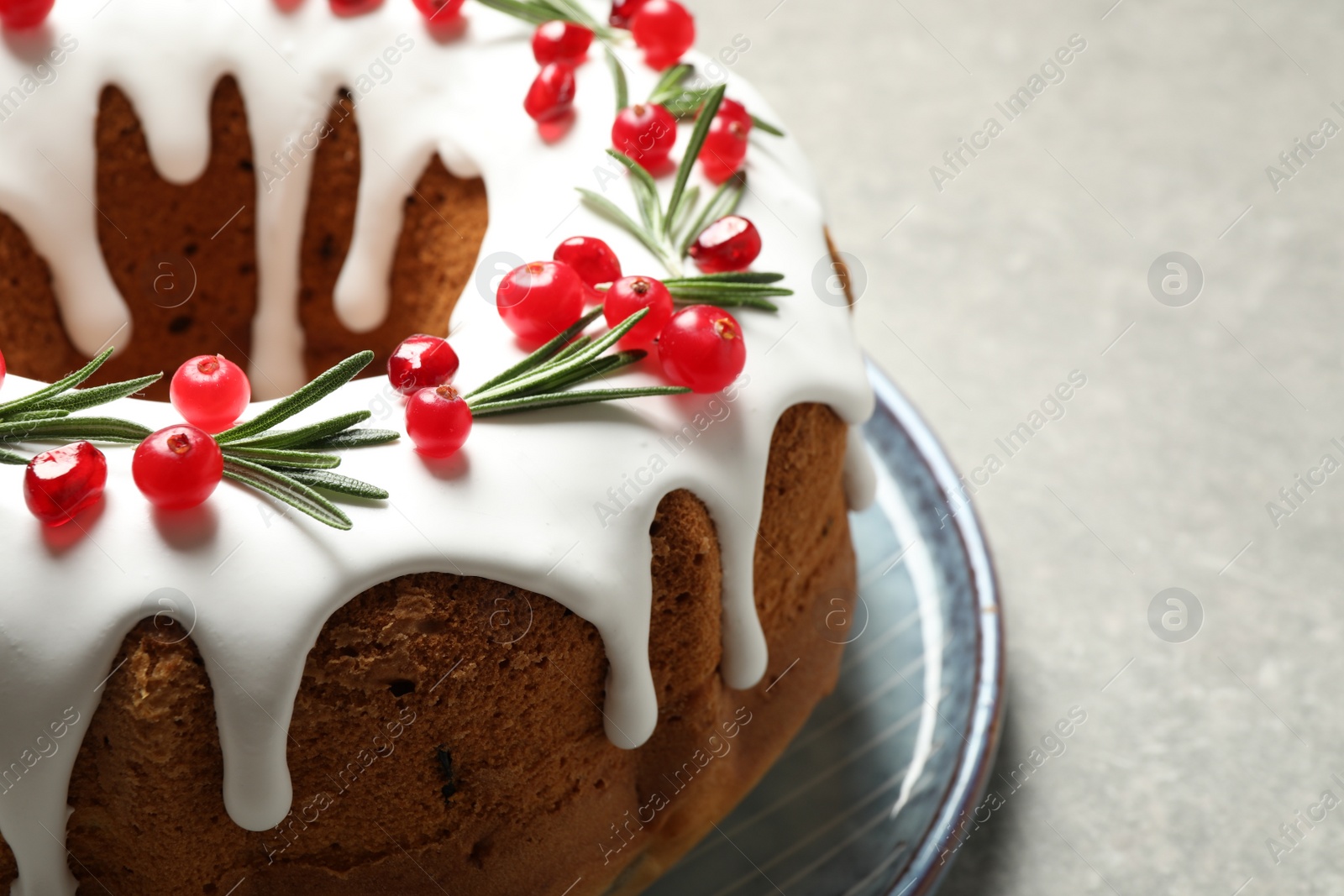 Photo of Traditional Christmas cake decorated with glaze, pomegranate seeds, cranberries and rosemary on light grey table, closeup