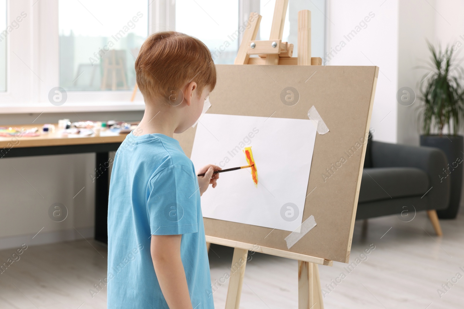 Photo of Little boy painting in studio, back view. Using easel to hold canvas