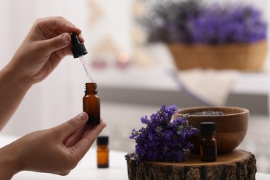 Photo of Woman with bottle of essential oil at table indoors, closeup